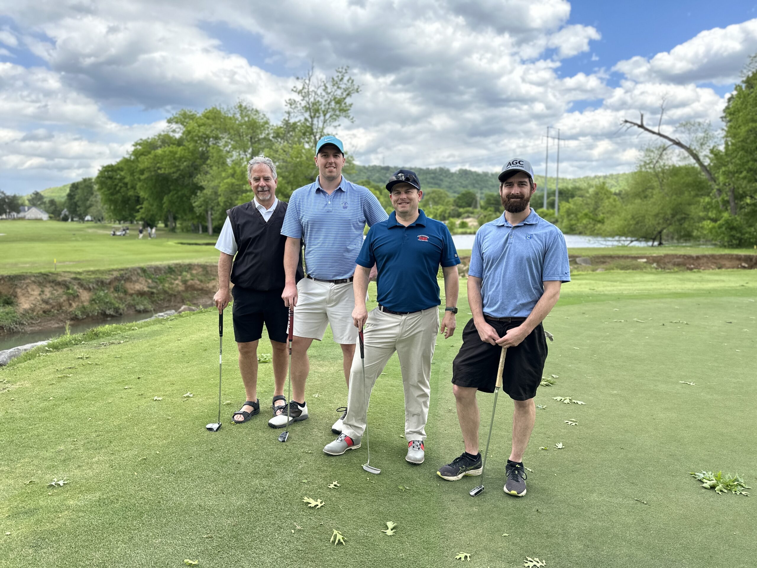 Four men posing on a golf course under a partly cloudy sky.